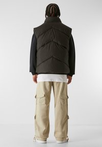 Donker groene puffer vest met chevron-quilting, gecombineerd met beige cargo pants met meerdere zakken en witte sneakers.
