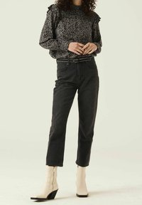 Blouse à manches longues noir et blanc à pois avec des épaulettes volantes, associée à un jean noir taille haute et des bottines crème à talon carré.