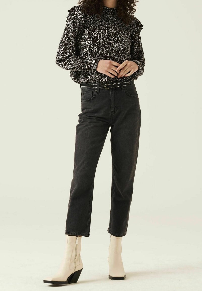 Blouse à manches longues noir et blanc à pois avec des épaulettes volantes, associée à un jean noir taille haute et des bottines crème à talon carré.