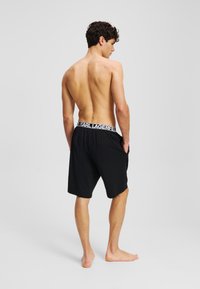Zwarte shorts van zacht materiaal met een elastische tailleband en de witte branding "KARL LAGERFELD". Model van achteren weergegeven.