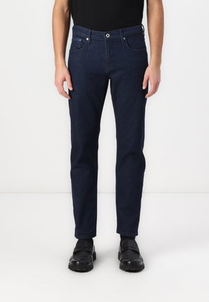 Dark blue denim jeans featuring a straight cut, five-pocket design, and a button closure; paired with black shoes.
