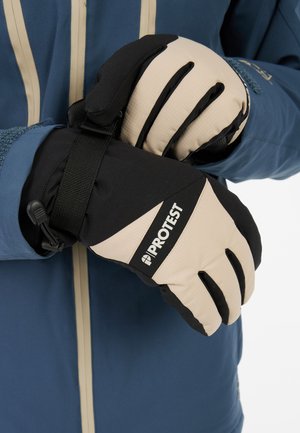 Gants noirs et beiges avec une finition texturée, présentant un logo, une bande réglable et des sections de doigts distinctes. Veste bleue en arrière-plan.