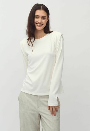 Witte top met lange mouwen en een ronde halslijn, voorzien van geplooide schouderdetails, gecombineerd met lichtgrijze, gestructureerde broeken. Soepele stoftextuur.