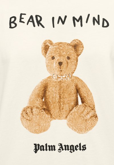 Κρεμ μπλουζάκι με γραφικό καφέ αρκουδάκι με υφασμάτινο σχέδιο, πάνω από το κείμενο "BEAR IN MIND" και κάτω από το "Palm Angels."