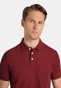 Bordowy polo z teksturowanej tkaniny, z krótkimi rękawami, zapięciem na trzy guziki i subtelnym logo na piersi.