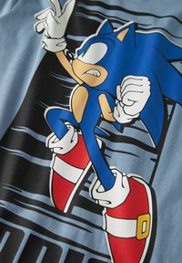 Maglietta blu con una grafica di un personaggio antropomorfo blu, con guanti bianchi e scarpe rosse, su uno sfondo nero e blu.