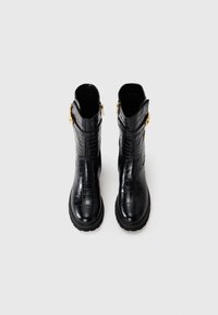 Botas de tobillo negras de cuero con estampado de cocodrilo, con punta redonda, cierre de cremallera y acentos de hardware en tono dorado. Suela de goma para tracción.