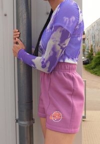 Lila tie-dye långärmad topp i kombination med korta rosa bomullsbyxor med en broderad logotyp på vänster ben. Båda är i avslappnad passform.