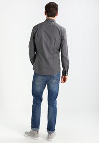 Grå langærmet skjorte med knaplukning ved kraven; kombineret med blå jeans og grå sneakers. Glat tekstur med tætsiddende design.