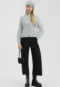 Šviesiai pilkas megztas kardiganas su sagutėmis, derinamas su pilku viršumi, juodomis plačiomis kelnėmis ir juodais platforminiais batais. Aksesuaras - mažas juodas rankinukas.