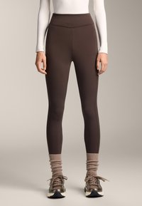 Bordeaux hoge taille leggings gemaakt van gladde, rekbare stof met contrasterende stiksels. Gecombineerd met grijze gewatteerde sokken en sportieve schoenen.