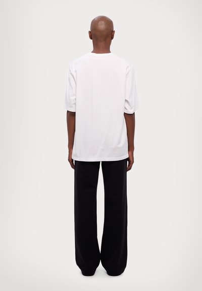 Weißes Baumwoll-T-Shirt mit lockerer Passform und kurzen Ärmeln, kombiniert mit lockeren schwarzen Hosen. Einfaches Design, keine sichtbaren Muster oder Akzente.