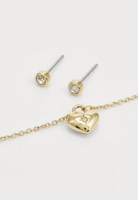 Goldenes Herz-Anhängerarmband mit einem kleinen Diamantakzent, begleitet von zwei goldenen Ohrsteckern mit klaren Edelsteinen.