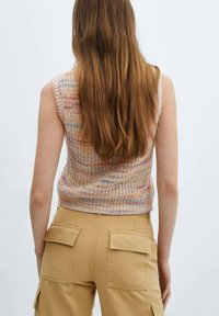 Strickärmloses Oberteil in sanften Farbtönen mit einem strukturierten Muster. Kombiniert mit beigen Cargo-Hosen, sichtbaren Gesäßtaschen und Nahtdetails.