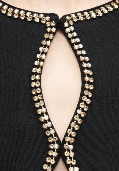 Μαύρο ένδυμα με λαιμόκοψη σε σχήμα δακρύου με περιβάλλονταν από δύο σειρές μικρών στρογγυλών χρυσών στρας.