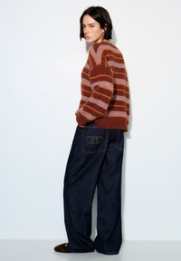 Gestreepte trui in roest- en roze tinten, gecombineerd met wijde donkerblauwe denim jeans met hartborduursels op de achterzakken.