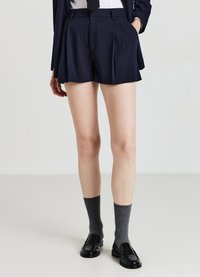 Pantaloni sartoriali navy a righe con pieghe, abbinati a calze grigie a coste e mocassini neri, presentano un design elegante.