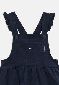 Tmavomodré kordové šaty s volánovými ramienkami, predné vrecko s logom Tommy Hilfiger a značkovým označením na hrudi.