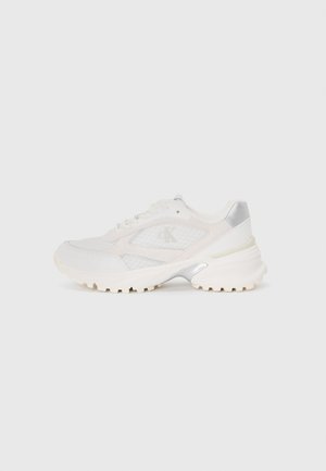 Scarpe sportive bianche realizzate in materiali in rete e pelle, con una suola testurizzata, dettagli argentati e un logo prominente sul lato.