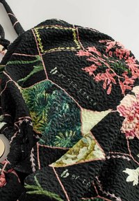 Crni cvjetni ruksak s teksturiranim kviltanim uzorkom, živopisnim zelenim i ružičastim detaljima te logo detaljem. Idealno za svakodnevnu upotrebu.