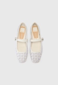 Ballerines blanches avec un motif découpé floral, présentant une sangle sur le cou-de-pied et un design à bout rond. Doublure intérieure douce.