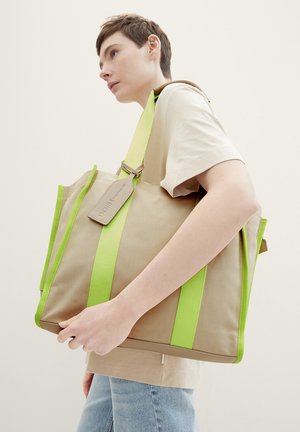 Beige Canvas-Tasche mit leuchtend grünen Trägern und Akzenten. Enthält ein Etikett mit geprägtem Text. Verfügt über ein geräumiges, rechteckiges Design.