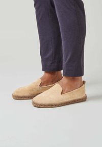 Espadrilles en suédé beige clair à enfiler avec une semelle en jute tissée. Le design présente une ouverture en V et une texture lisse.