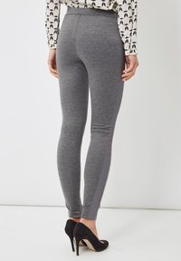 Leggings grises con una textura suave, que presentan una franja lateral en gris oscuro en contraste. Combinados con zapatos de tacón negros.