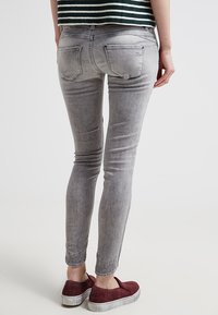 Jeans skinnies grises con un acabado deslavado, con dos bolsillos traseros y un ajuste ceñido, combinados con zapatos tipo slip-on burdeos.