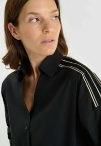Zwarte shirt met een klassieke kraag, voorzien van horizontale gestreepte accenten op de schouders. Glad textuur en getailleerde pasvorm.
