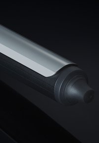 Barrel de fer à friser métallique avec une pointe résistante à la chaleur noire sur une surface réfléchissante sombre.