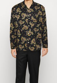 Camisa negra de manga corta con un colorido patrón de paisley, hecha de una tela suave, con cierre de botones en la parte delantera y un bolsillo en el pecho.