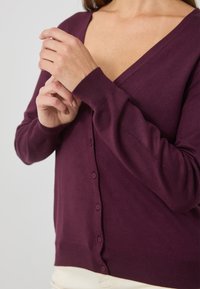 V-Ausschnitt, langärmelige Strickjacke in tiefem Lila, mit Knopfleiste und gerippten Bündchen, aus weichem Strickmaterial gefertigt.