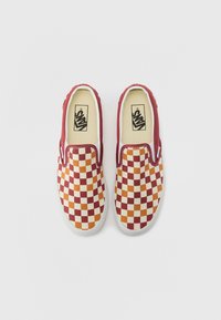 Red and orange checkerboard slip-on shoes with white soles and fabric upper. Vans logo visible on the insole. Smooth texture, casual design.