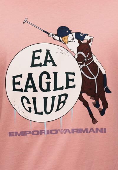 Παίκτης πόλο με κεφάλι αετού πάνω σε άλογο κουνάει το μαλέτι προς μια μεγάλη μπάλα με την επιγραφή «EA Eagle Club», και από κάτω το «Emporio Armani» σε ροζ φόντο.