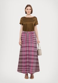 Blusa di raso marrone con scollo tondo, abbinata a una lunga gonna tartan multicolore con tonalità di rosa, viola e marrone.