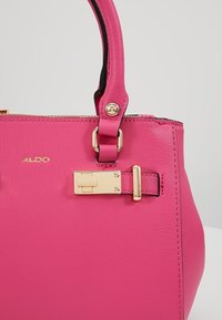 Sac à main texturé rose vif avec détail de serrure en métal doré et poignée rose assortie, avec le nom de la marque Aldo en lettres dorées.