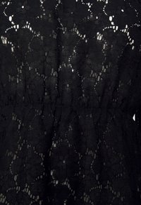 Svart spetsklänning med ett blommönster, med en samla midja och genomskinlig textur som avslöjar huden under.