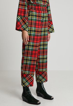 Dolna część ciała osoby noszącej czerwone, zielone, żółte i czarne spodnie w kratę z pasującymi długimi rękawami oraz czarne lakierowane botki na kostkę.