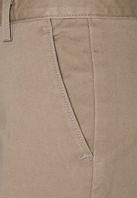 Närbild på beige tyg som visar en jämn textur, fina ribbor, sidofickans söm och kontrasterande sömnad längs kanterna.