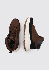 Botas altas marrones y negras que cuentan con una parte superior texturizada, suela de goma y diseño con cordones. Los acentos destacados incluyen un cuello acolchado y una lengüeta.