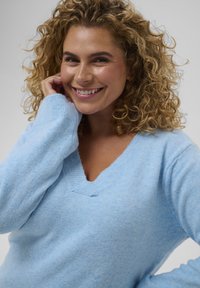 Pull bleu clair en maille douce avec un col en V et des manches longues, présentant une coupe décontractée et une texture subtile.