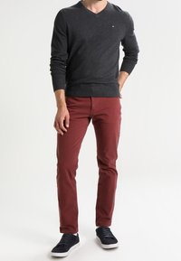 Tummanharmaa V-kaula-aukkoinen neule, slim-fit burgundin väriset housut ja tummansiniset lenkkarit. Neuleessa on ribbineulos hihasuissa ja pieni logo rinnassa.