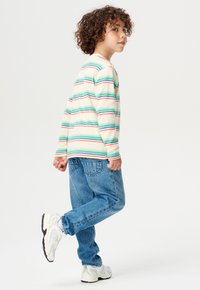 Chemise à rayures à manches longues en crème, vert, bleu et orange, associée à un jean en denim bleu et à des baskets blanches avec des accents gris.