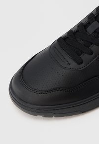 Czarne sportowe sneakersy z teksturowaną skórzaną cholewką, okrągłym noskiem i sznurowanym zapięciem; zawierają perforowane detale po bokach.
