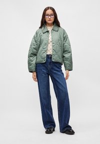 Πράσινο ραμμένο μπουφάν με γιακά και κλείσιμο με κουμπάκια, φορεμένο πάνω από μια κρέμα δαντελωτή μπλούζα. Συνδυασμένο με χαλαρά μπλε τζιν και μαύρα παπούτσια.