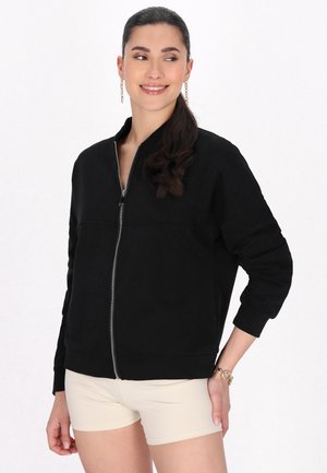 Giacca bomber nera con zip in tessuto morbido, dotata di colletto alto, maniche lunghe e polsini a coste. Texture liscia con un design minimalista.