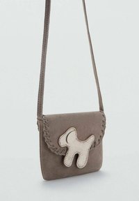 Borsa a tracolla in suede grigio con bordi cuciti, caratterizzata da un accento a forma di cane di colore crema sulla parte anteriore. Include una tracolla regolabile.