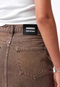 Jeans de mezclilla marrón con un acabado texturizado, que cuentan con una etiqueta negra de DRDENIM en la parte posterior de la cinturilla y un bolsillo trasero en el lado derecho.