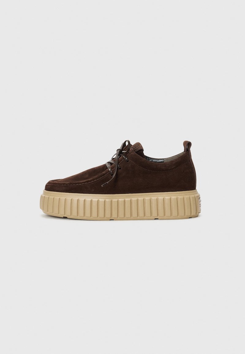 Chaussures en daim brun avec une semelle crantée épaisse de couleur crème. Elles présentent un bout arrondi et des lacets bruns. L'arrière possède une petite boucle pour un enfilage facile.